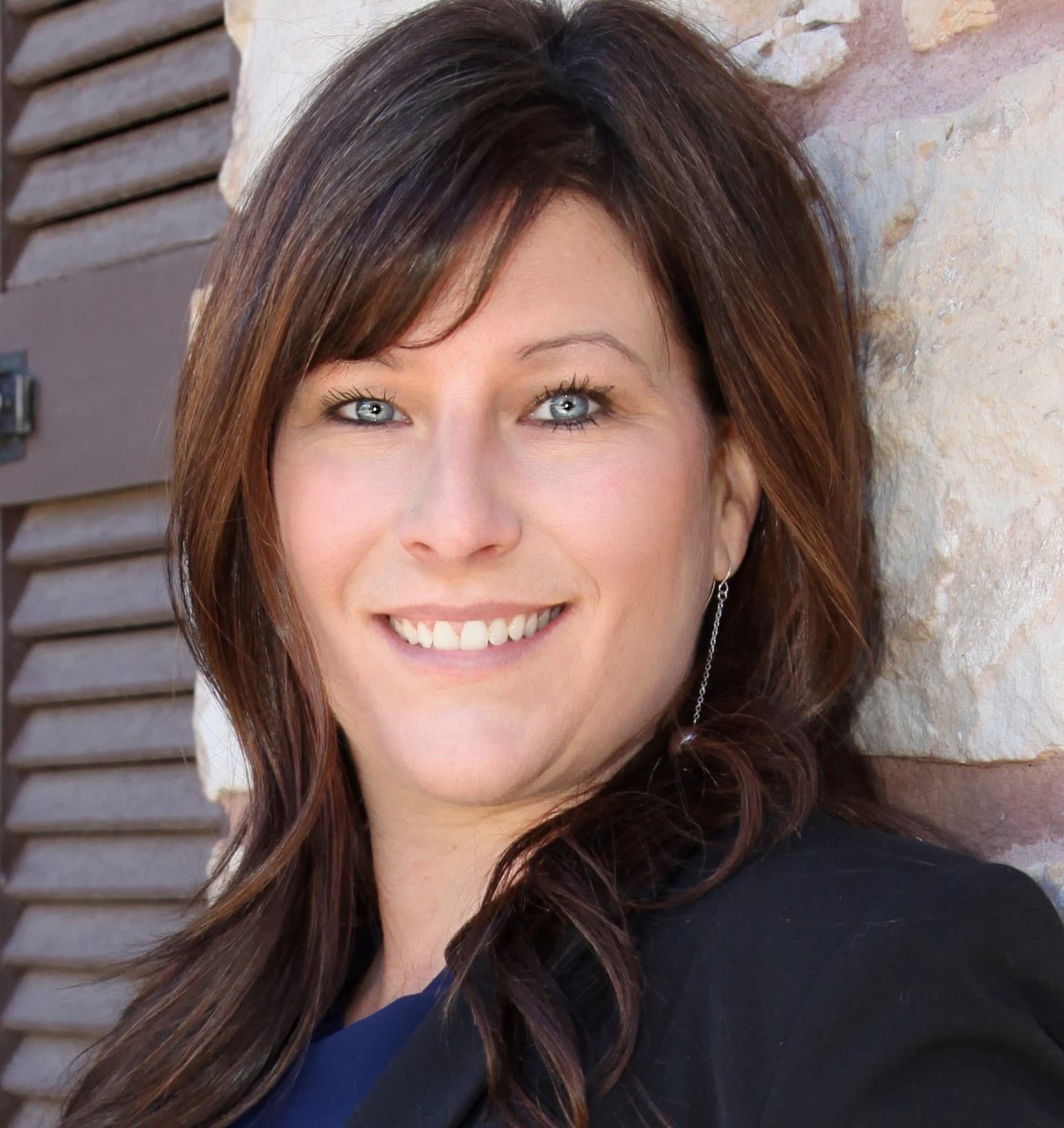 Krista N. Kaufmann, CDFA®, smiling in front of a stone wall and wooden shutters